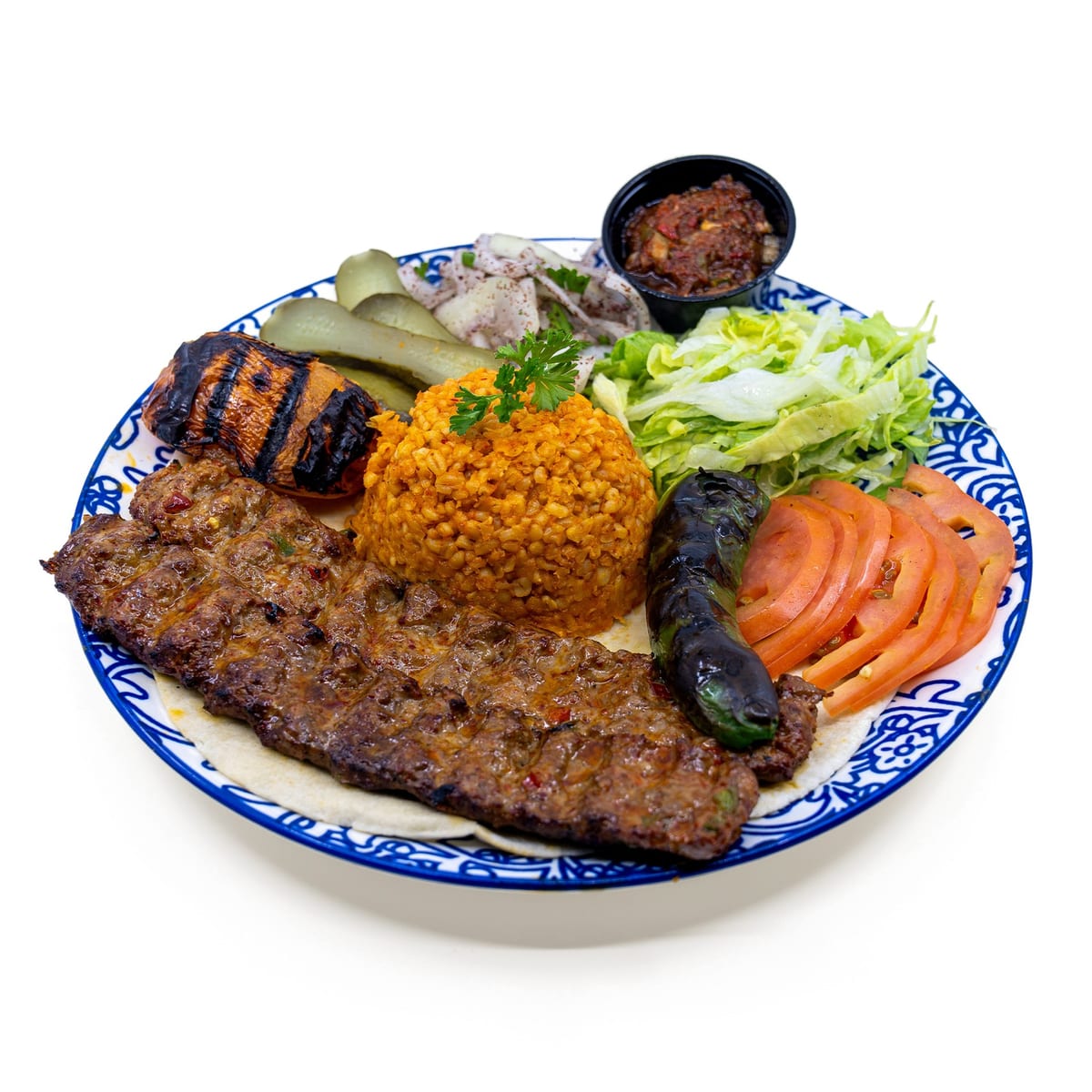 Adana kebab plate with rice, grilled tomato and pepper, salad and pickles